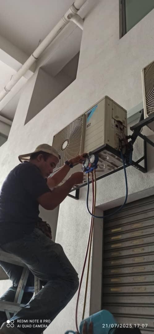 Juruteknik mengambil bacaan tekanan gas aircond menggunakan gauge pada unit luar